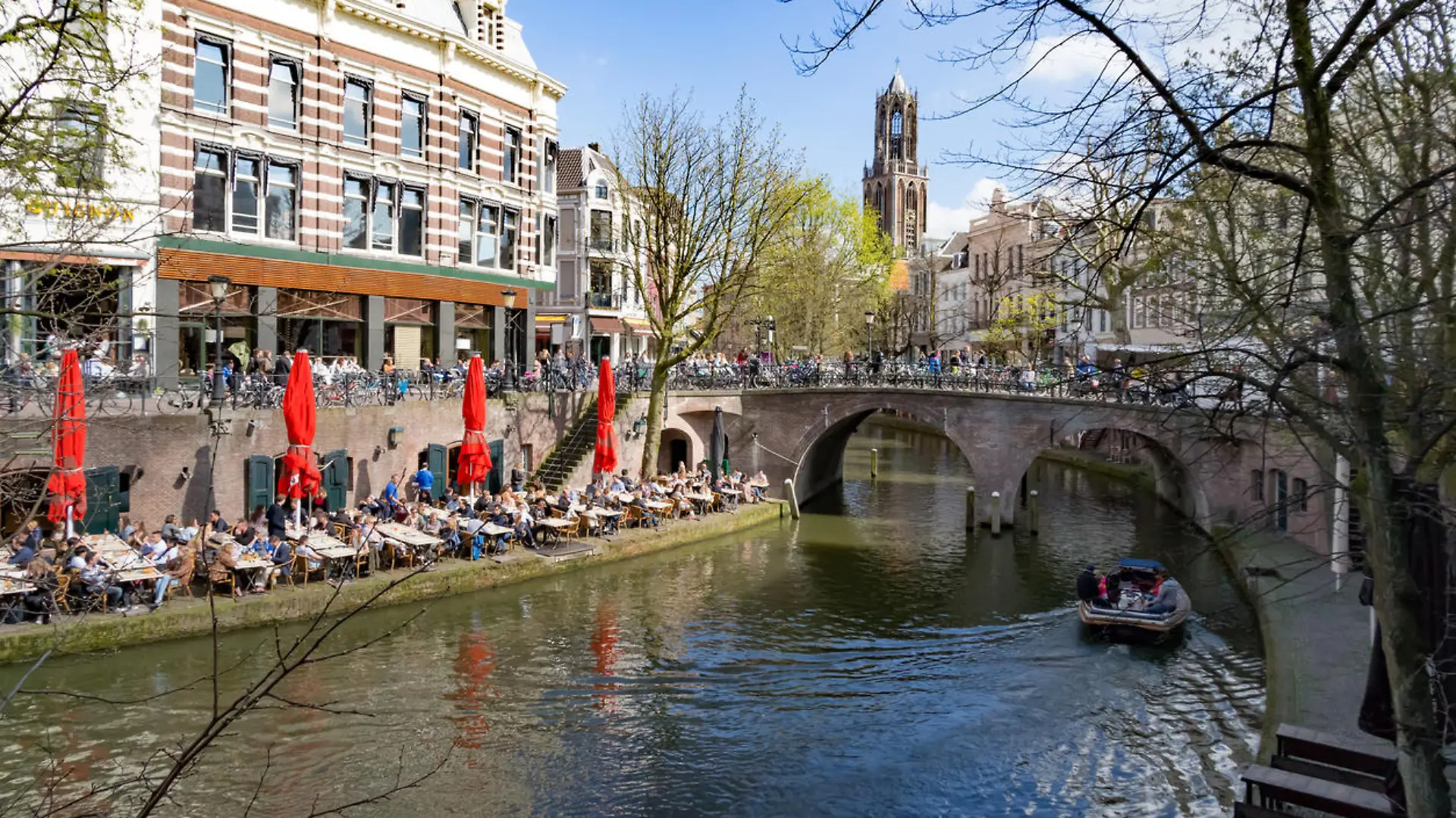All tables at the terraces along the canals in Utrecht are occupied on the first sunny sunday in spring. Many tourist visit this city in The Netherlands. The shops and houses are mostly located  ancient buildings with a nice view on the water. In the background the famous Dom Toren.