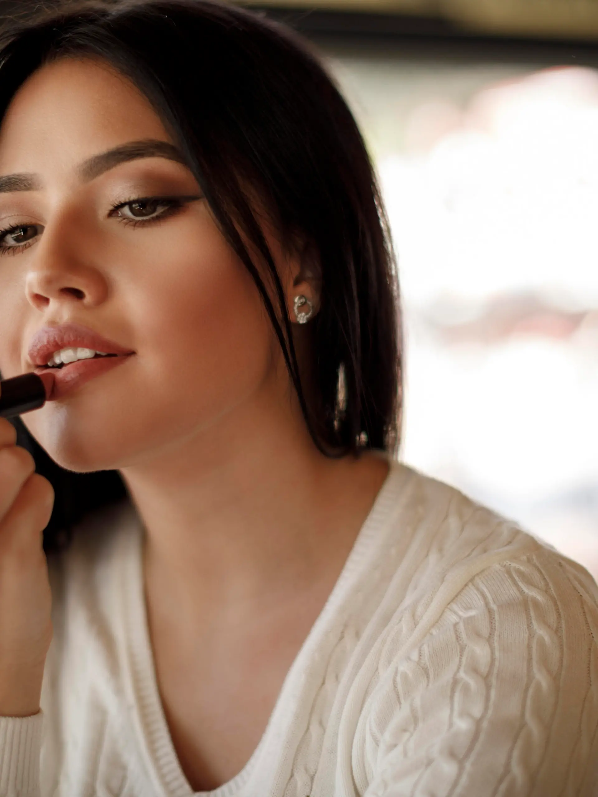 Young woman applying lipstick at a cafe