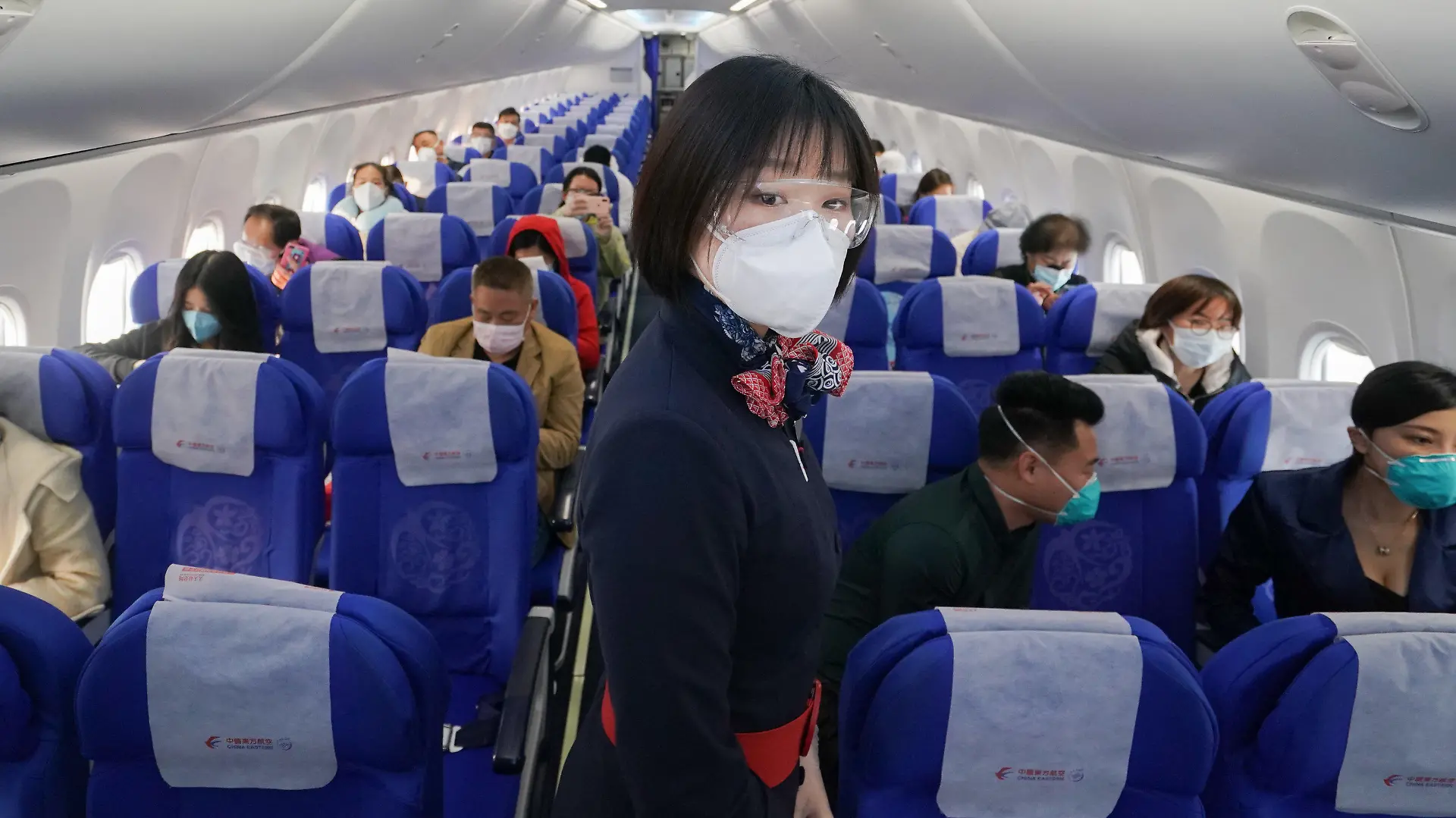 08.04.2020, China, Wuhan: Eine Flugbegleiterin mit Mundschutz steht an Bord des Fluges MU2627 vom Internationalen Flughafen Wuhan-Tianhe zwischen den Passagieren. Die Reisebeschränkungen in der Stadt wurden nach fast 11 Wochen wieder aufgehoben. Foto: Cheng Min/XinHua/dpa +++ dpa-Bildfunk +++