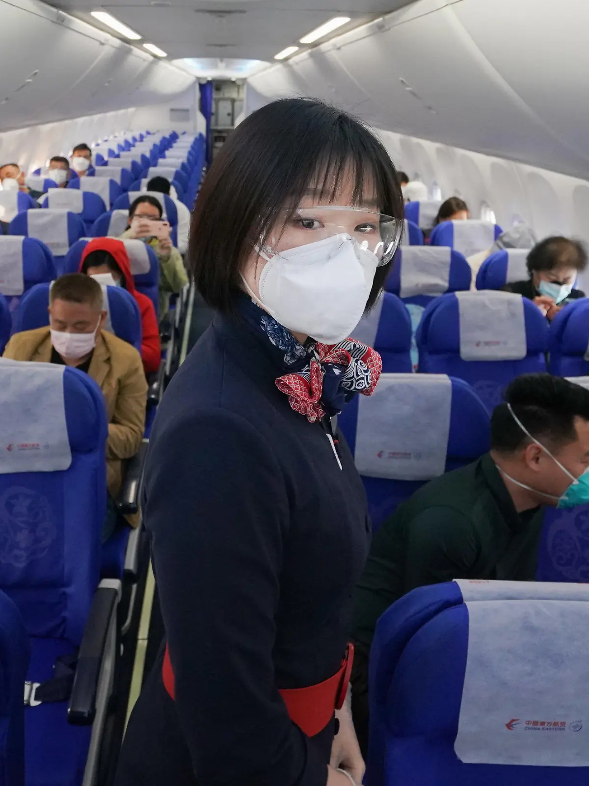 08.04.2020, China, Wuhan: Eine Flugbegleiterin mit Mundschutz steht an Bord des Fluges MU2627 vom Internationalen Flughafen Wuhan-Tianhe zwischen den Passagieren. Die Reisebeschränkungen in der Stadt wurden nach fast 11 Wochen wieder aufgehoben. Foto: Cheng Min/XinHua/dpa +++ dpa-Bildfunk +++