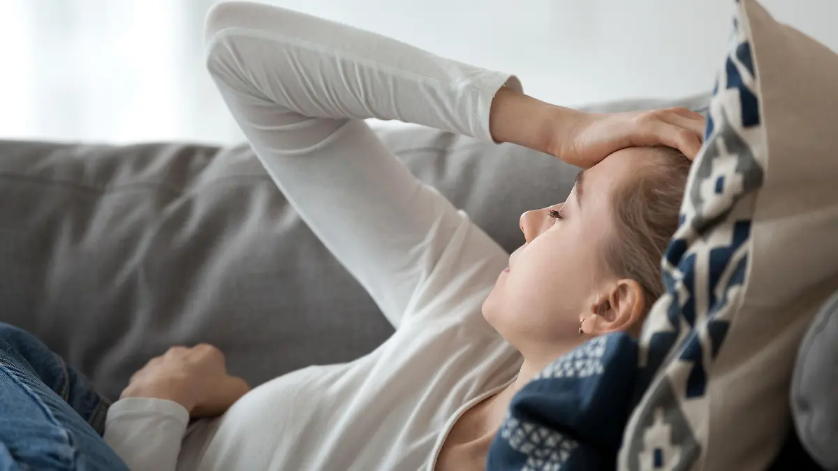 Upset depressed young woman lying on couch feeling strong headache migraine, sad tired drowsy teenager exhausted girl resting trying to sleep after nervous tension and stress, somnolence concept