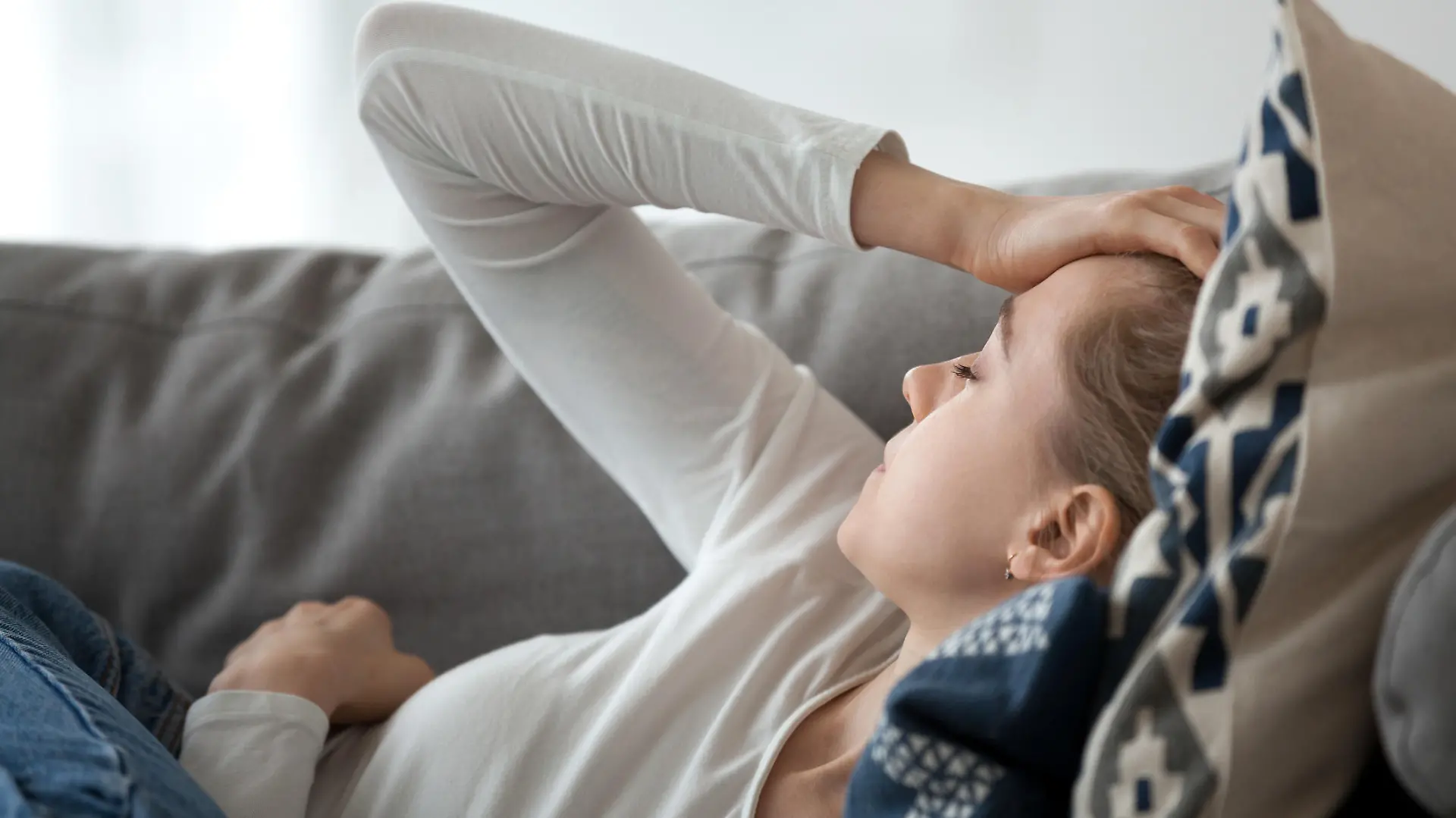 Upset depressed young woman lying on couch feeling strong headache migraine, sad tired drowsy teenager exhausted girl resting trying to sleep after nervous tension and stress, somnolence concept