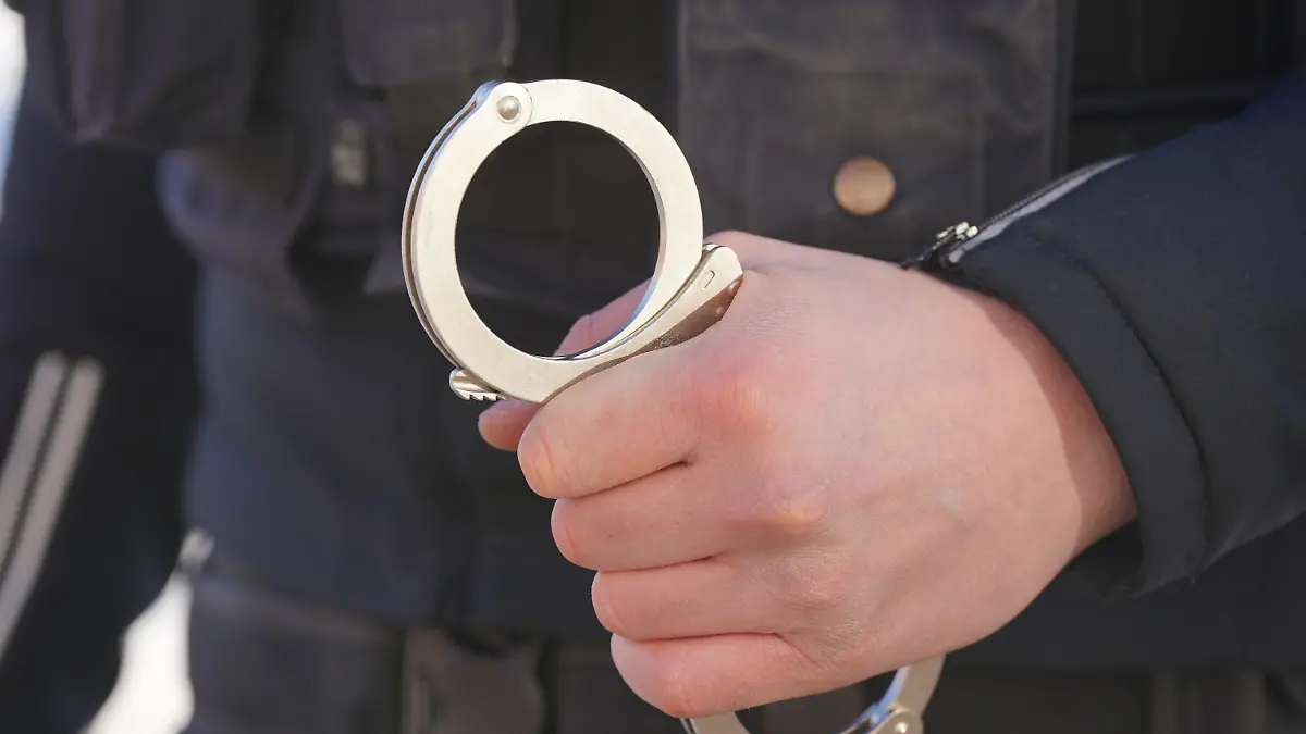 ARCHIV - 18.01.2024, Mecklenburg-Vorpommern, Schwerin: ILLUSTRATION - Ein Polizist hält Handschellen in der Hand. Ein Autohändler aus Frankfurt wurde verhaftet, weil er betrogen haben soll. (zu dpa: «Autohändler wegen Betrugsverdachts verhaftet») Foto: Marcus Brandt/dpa +++ dpa-Bildfunk +++