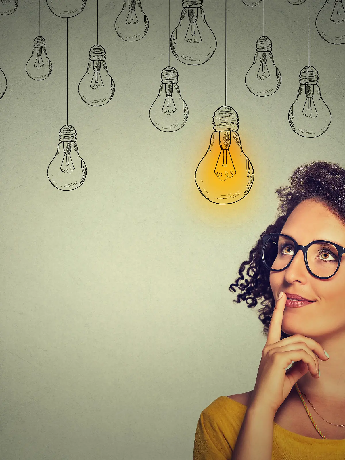 Portrait thinking woman in glasses looking up with light idea bulb above head isolated on gray wall background