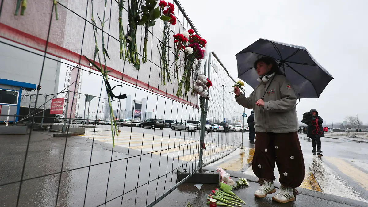 23.03.2024, Russland, Moskau: Eine Frau legt Blumen an einem Zaun nieder. Bei dem Anschlag auf das Veranstaltungszentrum Crocus City Hall ist die Zahl der Toten nach Angaben der Ermittler weiter gestiegen. Foto: Vitaly Smolnikov/AP/dpa +++ dpa-Bildfunk +++