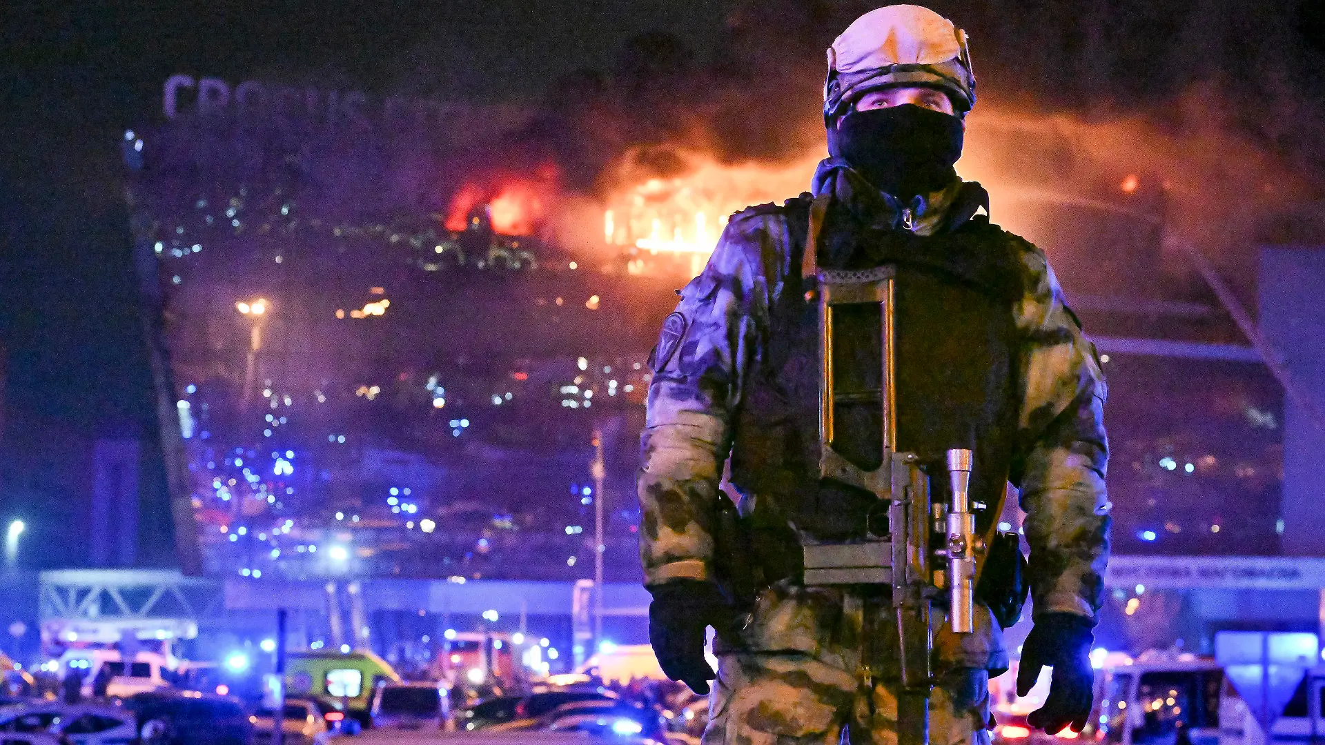 dpatopbilder - 22.03.2024, Russland, Moskau: Ein Soldat der russischen Nationalgarde (Rosgwardija) sichert ein Gebiet, während über Crocus City Hall am westlichen Rand Moskaus ein gewaltiger Brand zu sehen ist. Nach dem Angriff auf eine Veranstaltungshalle in der Region Moskau hat der russische Inlandsgeheimdienst FSB laut Agentur Interfax Tote und Verletzte bestätigt. Konkrete Zahlen zu dem mutmaßlichen Terroranschlag wurden am Freitagabend zunächst nicht genannt. Nach Behördenangaben wurden nach Schüssen und einem Brand weitere Explosionen gemeldet. Foto: Dmitry Serebryakov/AP +++ dpa-Bildfunk +++