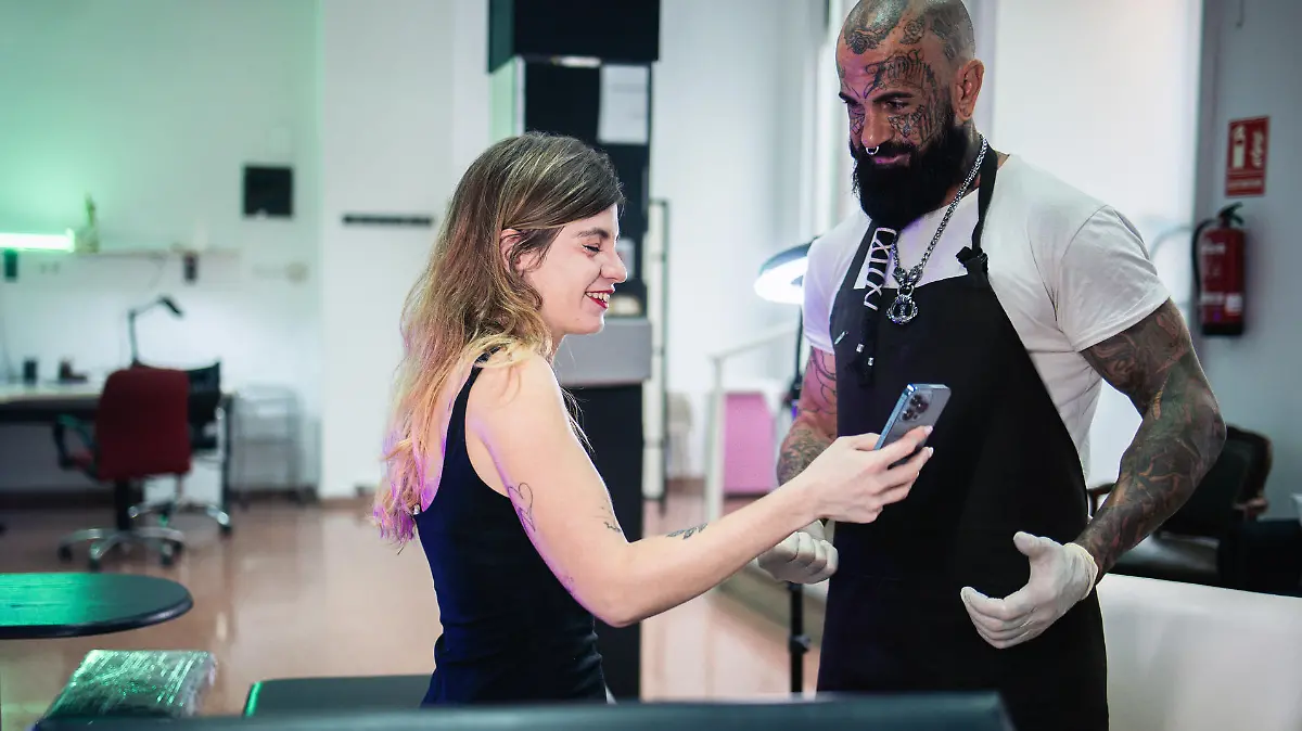 Young woman talking with a tattoo artist and showing to him on smartphone what kind of tattoo she wants.