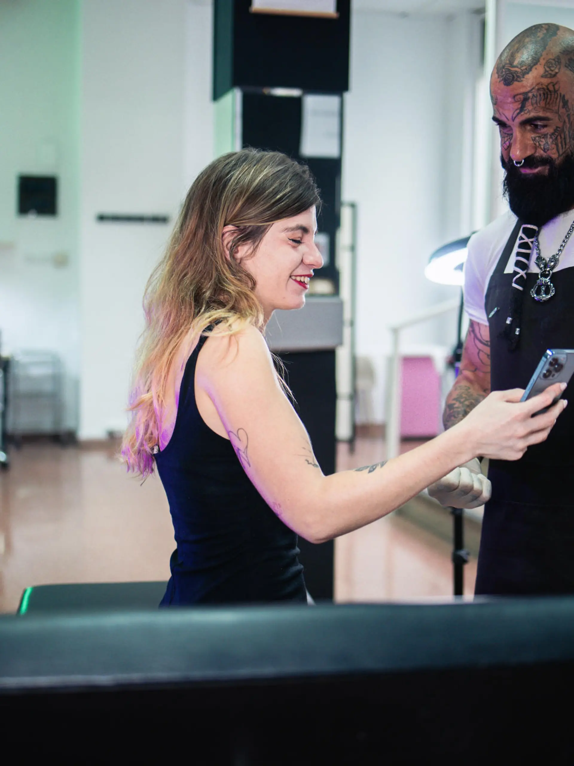 Young woman talking with a tattoo artist and showing to him on smartphone what kind of tattoo she wants.