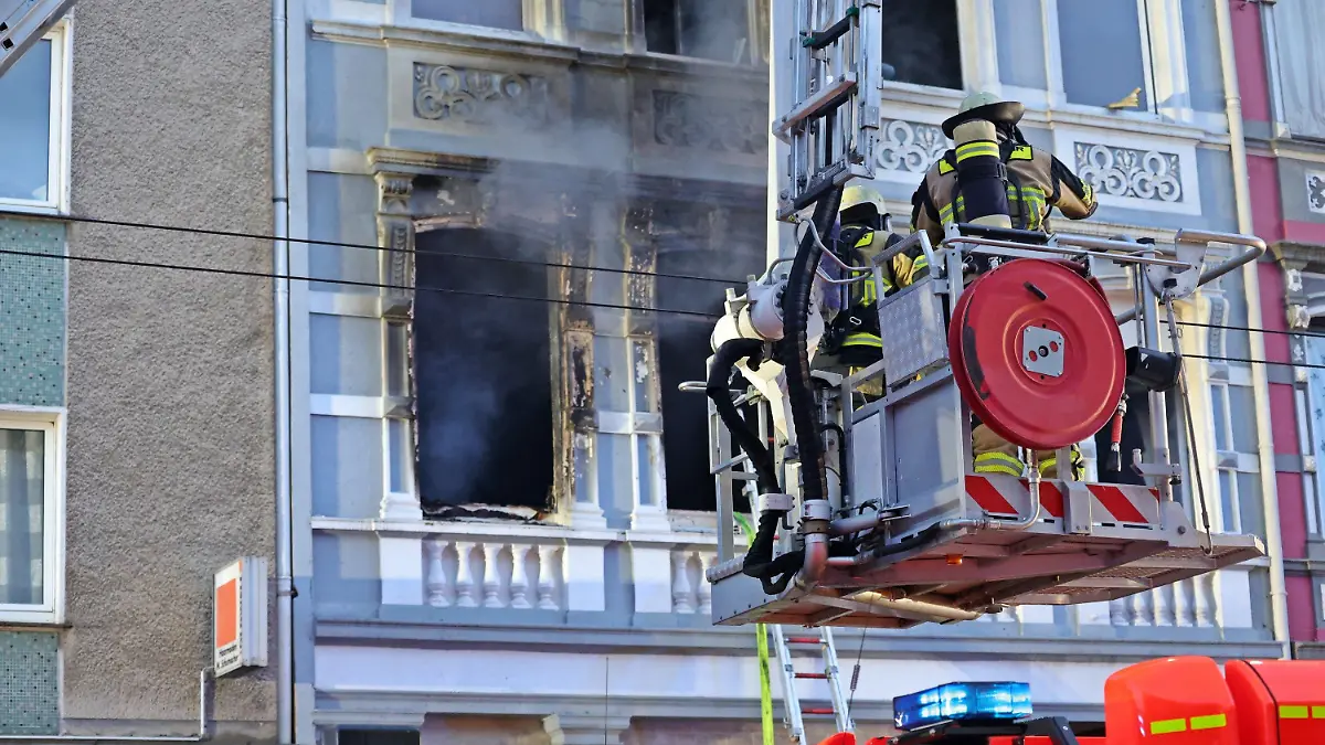 25.03.2024, Nordrhein-Westfalen, Solingen: Feuerwehrmänner stehen vor einem Mehrfamilienhaus, in dem es gebrannt hat, im Korb einer Drehleiter. Bei dem Wohnungsbrand am frühen Montagmorgen sind drei Menschen getötet worden, darunter ein Kind. Foto: Gianni Gattus/Blaulicht Solingen/dpa +++ dpa-Bildfunk +++