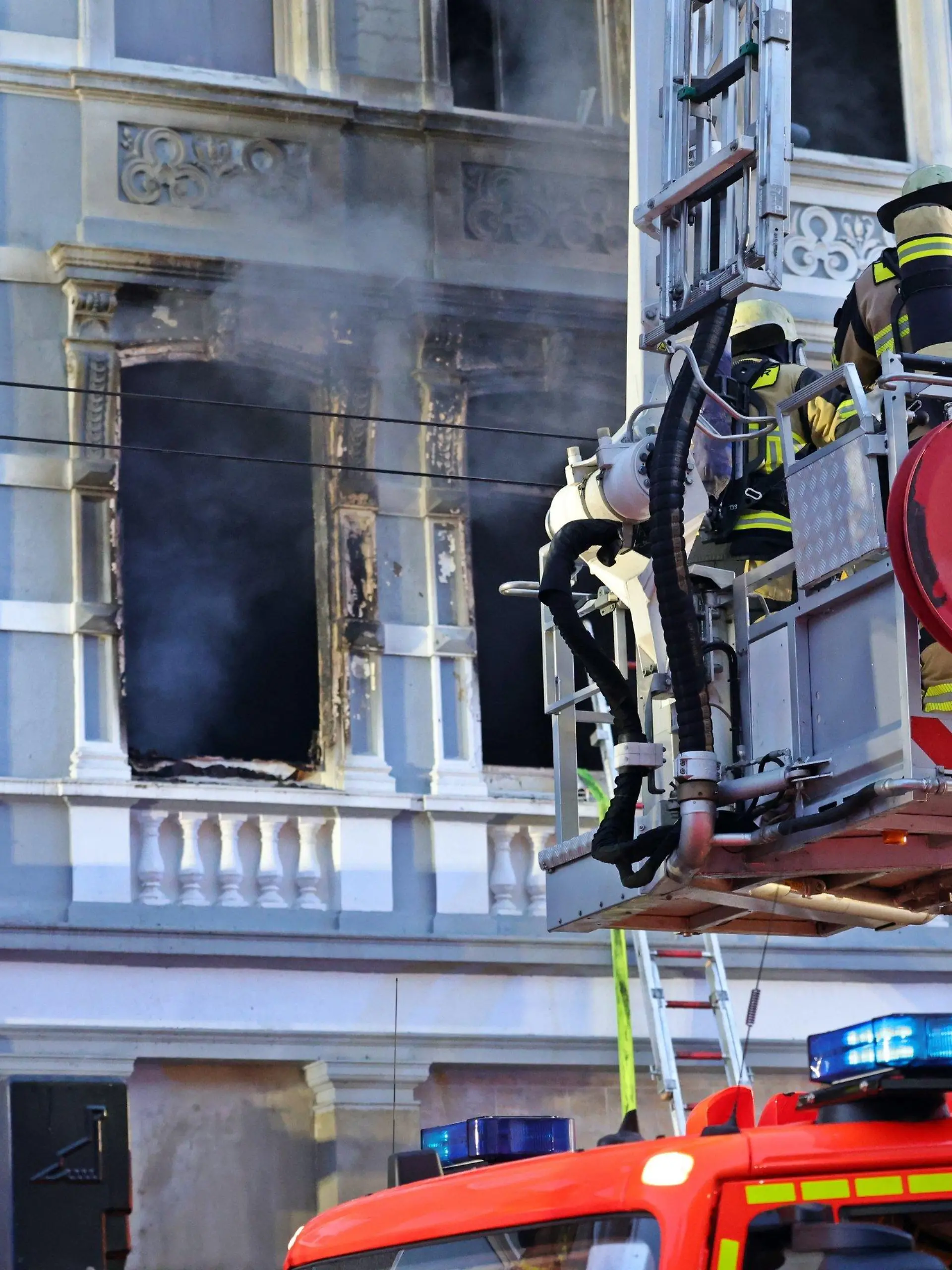 25.03.2024, Nordrhein-Westfalen, Solingen: Feuerwehrmänner stehen vor einem Mehrfamilienhaus, in dem es gebrannt hat, im Korb einer Drehleiter. Bei dem Wohnungsbrand am frühen Montagmorgen sind drei Menschen getötet worden, darunter ein Kind. Foto: Gianni Gattus/Blaulicht Solingen/dpa +++ dpa-Bildfunk +++
