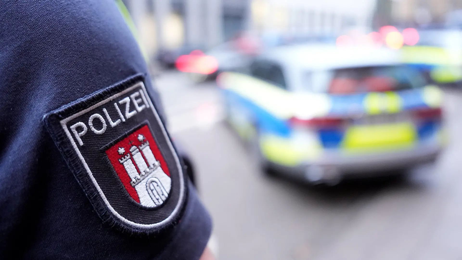 ARCHIV - 15.03.2024, Hamburg: ILLUSTRATION - Ein Polizist steht vor einem Einsatzfahrzeug der Polizei. (zu dpa: «Kleiner, dicker, älter: Hamburgs Polizei ändert Anforderungsprofil») Foto: Marcus Brandt/dpa +++ dpa-Bildfunk +++