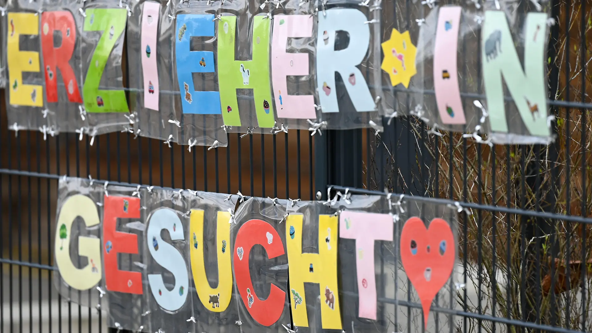 ILLUSTRATION - 10.02.2023, Hessen, Frankfurt/Main: Mit bunten Buchstaben sind die Worte ·Erzieher*in gesucht· geformt, die an einem Zaun einer Kindertagesstätte im Stadtteil Sachsenhausen befestigt sind. (zu dpa: «Brandbrief beklagt bayerischen Quereinstieg in Kitas») Foto: Arne Dedert/dpa +++ dpa-Bildfunk +++