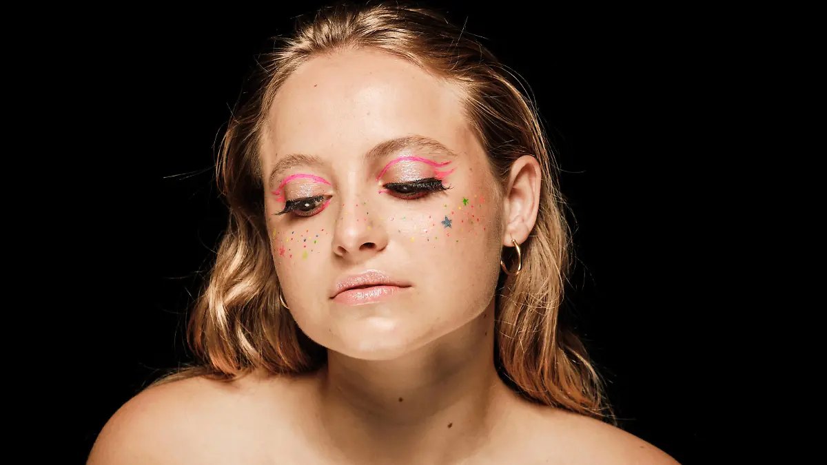 Charming female model with colorful makeup and bare shoulder looking down while standing against black background in modern studio ManuelOrts_BeautyPortraits_2.jpg Copyright: xManuelxOrtsx