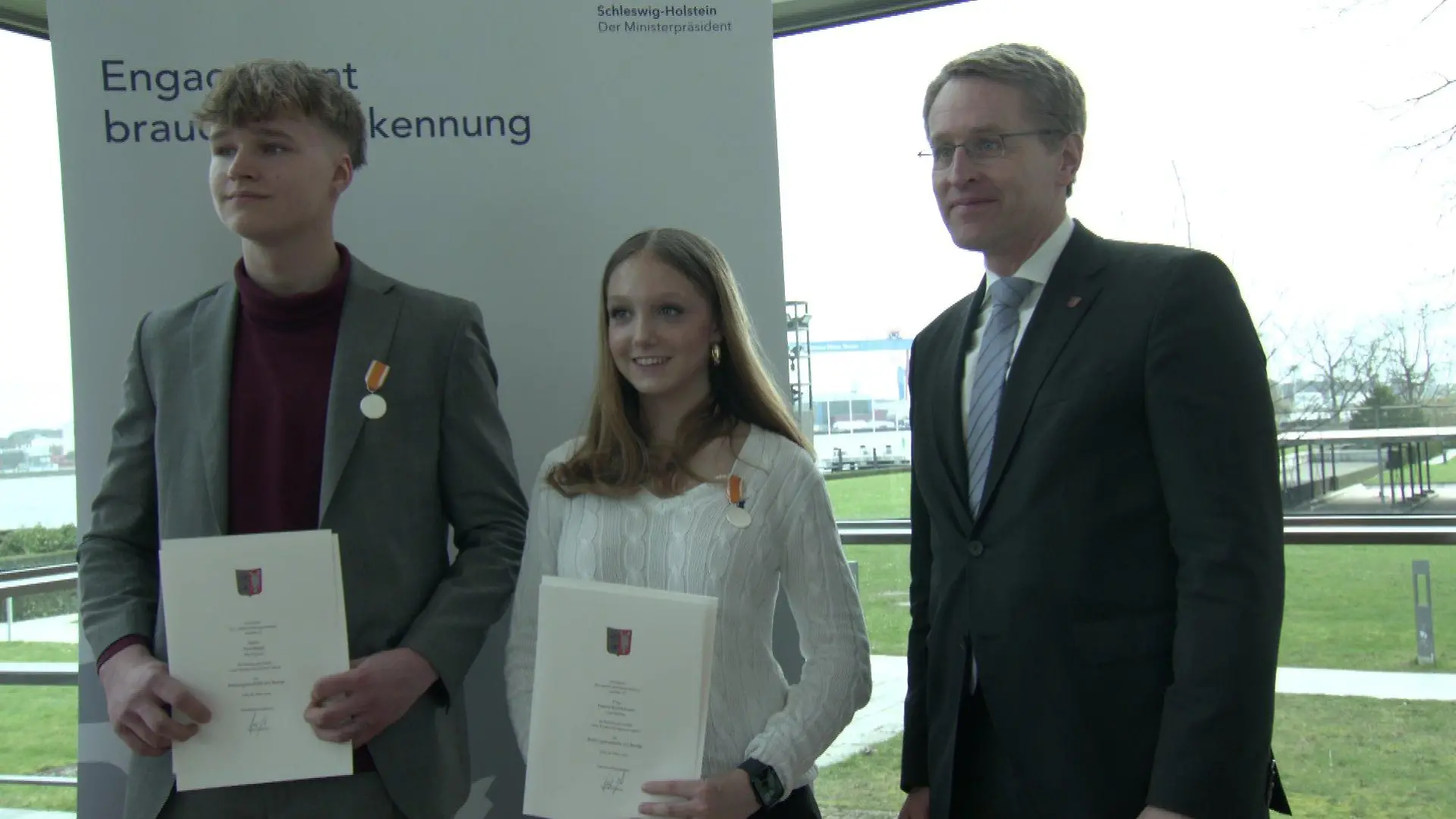 Hanna und Paul erhalten von Ministerpräsident Daniel Günther die Rettungsmedaille am Bande.
