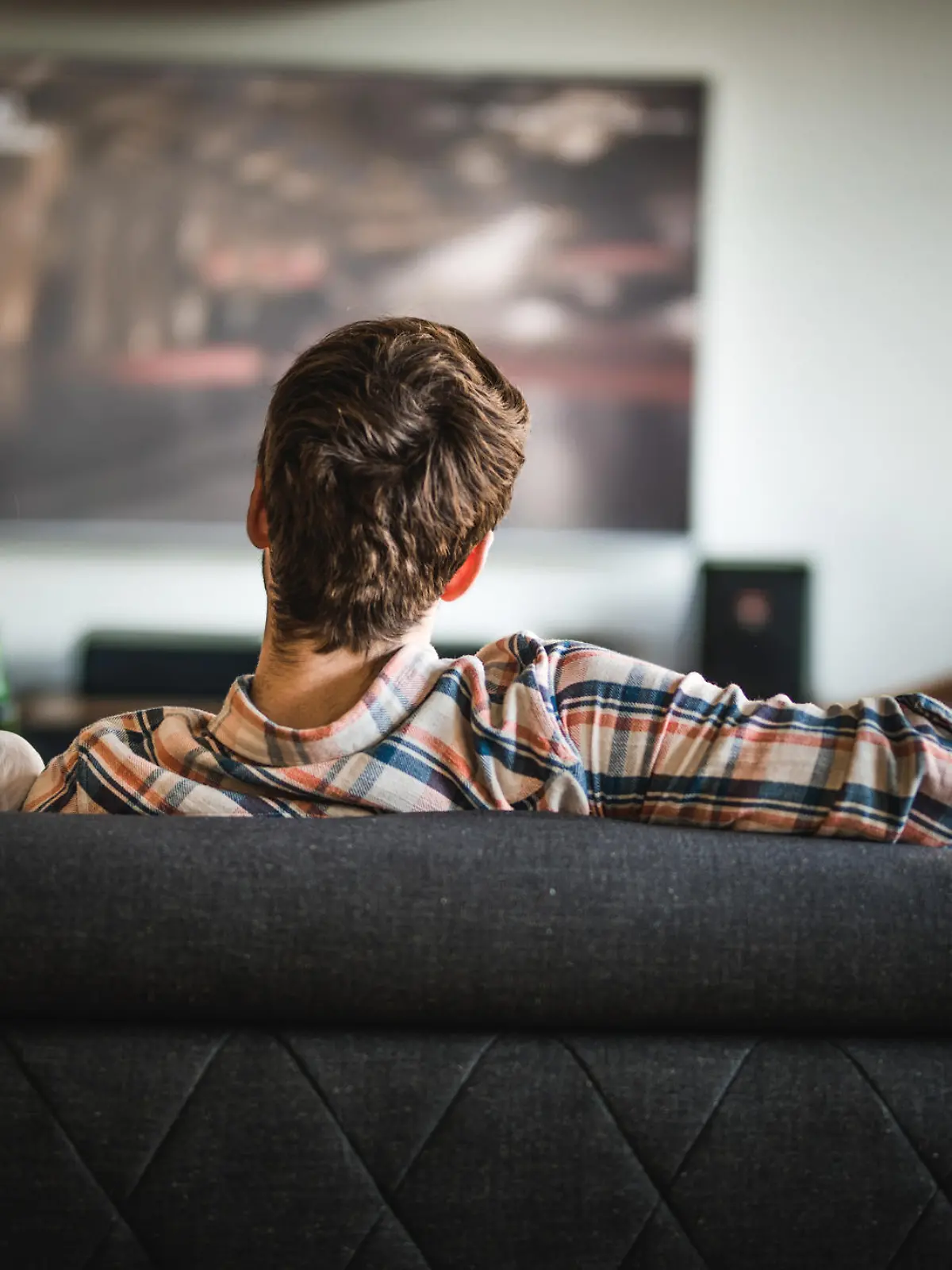 Rear view of a couple relaxing on sofa in the living room and watching a movie on TV.