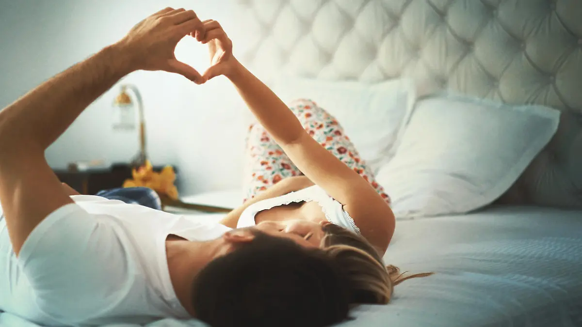 Closeup low angle shot of a partially unrecognizable  mid 20's loving couple relaxing in bed, cuddling and making hearts with their fingers. Toned image.