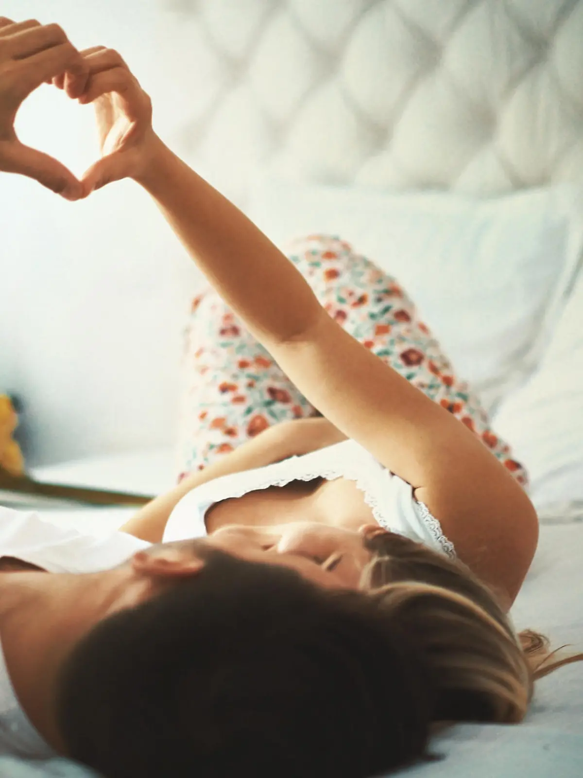 Closeup low angle shot of a partially unrecognizable  mid 20's loving couple relaxing in bed, cuddling and making hearts with their fingers. Toned image.