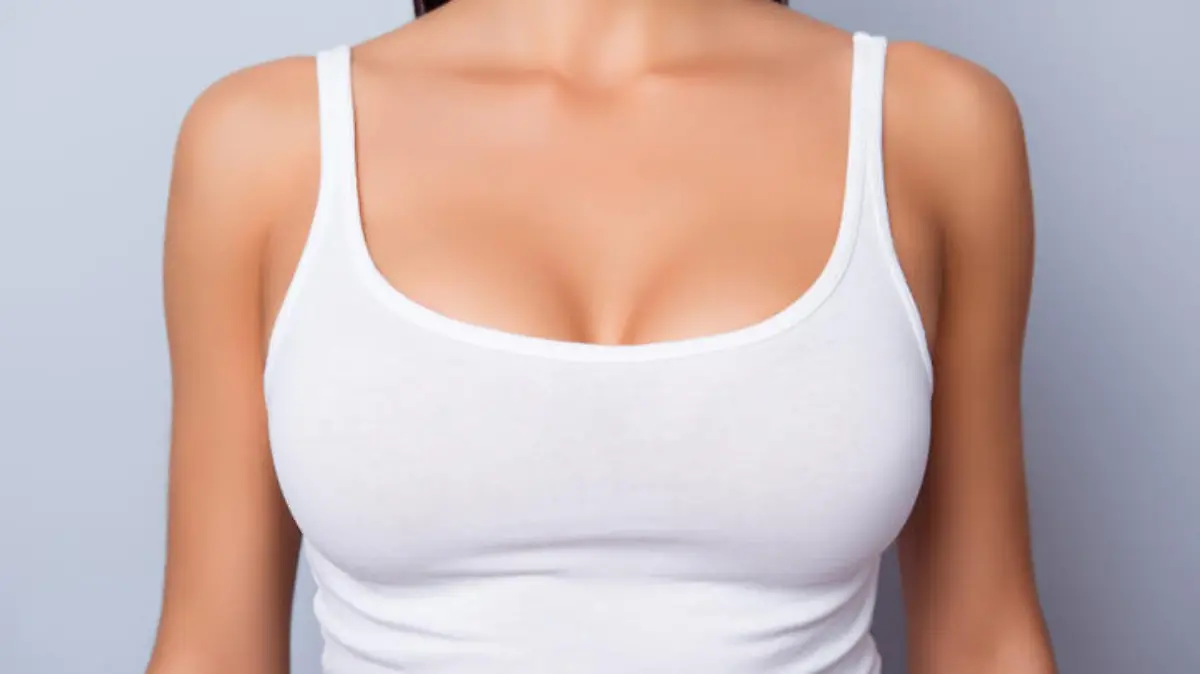Close up of perfect lady`s chest with bronze skin in white singlet on light blue background