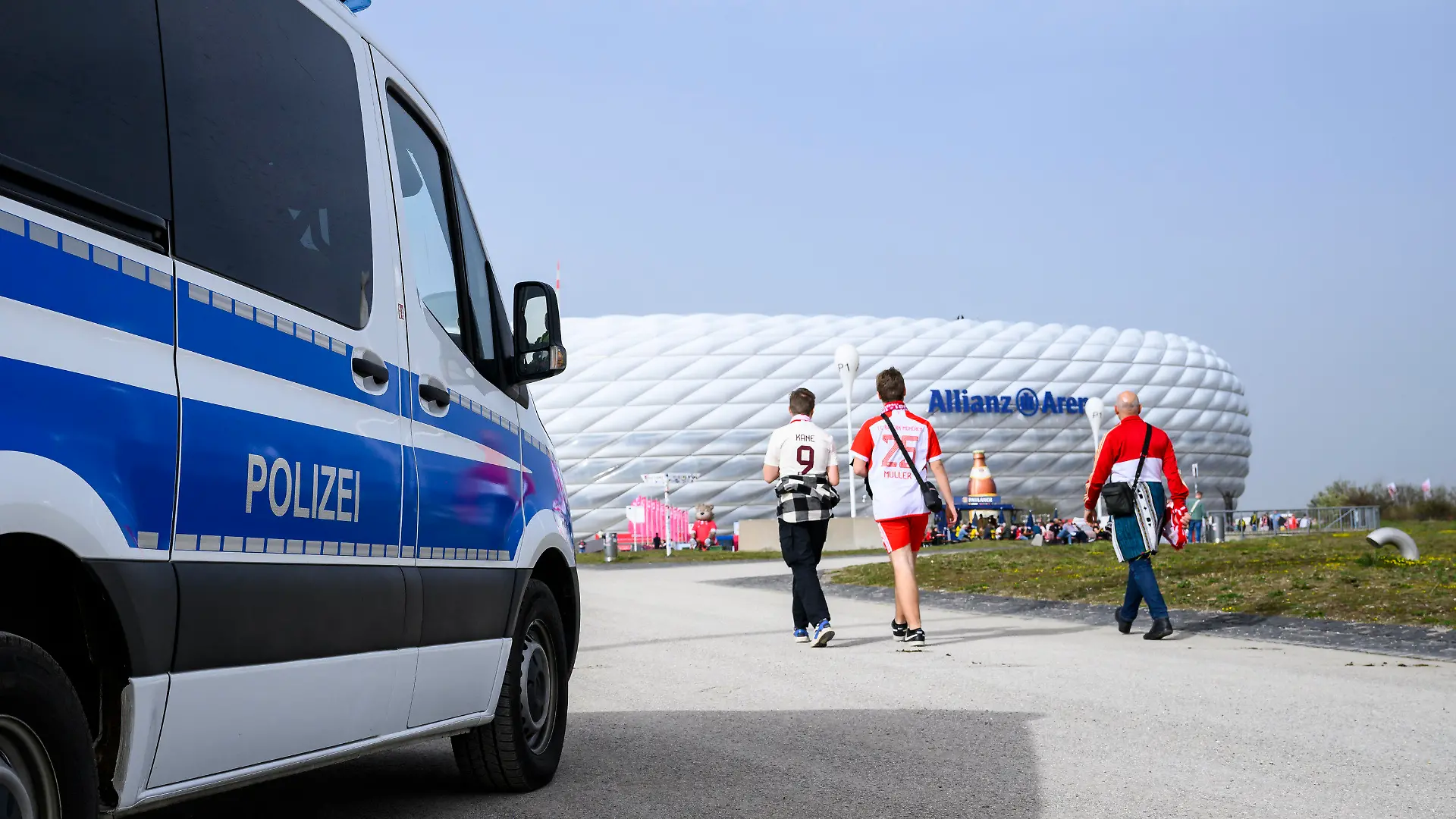 dpatopbilder - 30.03.2024, Bayern, München: Fußball: Bundesliga, Bayern München - Borussia Dortmund, 27. Spieltag, Allianz Arena. Fans gehen neben einem Auto der Polizei vor dem Spiel in die Allianz Arena. Foto: Tom Weller/dpa - WICHTIGER HINWEIS: Gemäß den Vorgaben der DFL Deutsche Fußball Liga bzw. des DFB Deutscher Fußball-Bund ist es untersagt, in dem Stadion und/oder vom Spiel angefertigte Fotoaufnahmen in Form von Sequenzbildern und/oder videoähnlichen Fotostrecken zu verwerten bzw. verwerten zu lassen. +++ dpa-Bildfunk +++