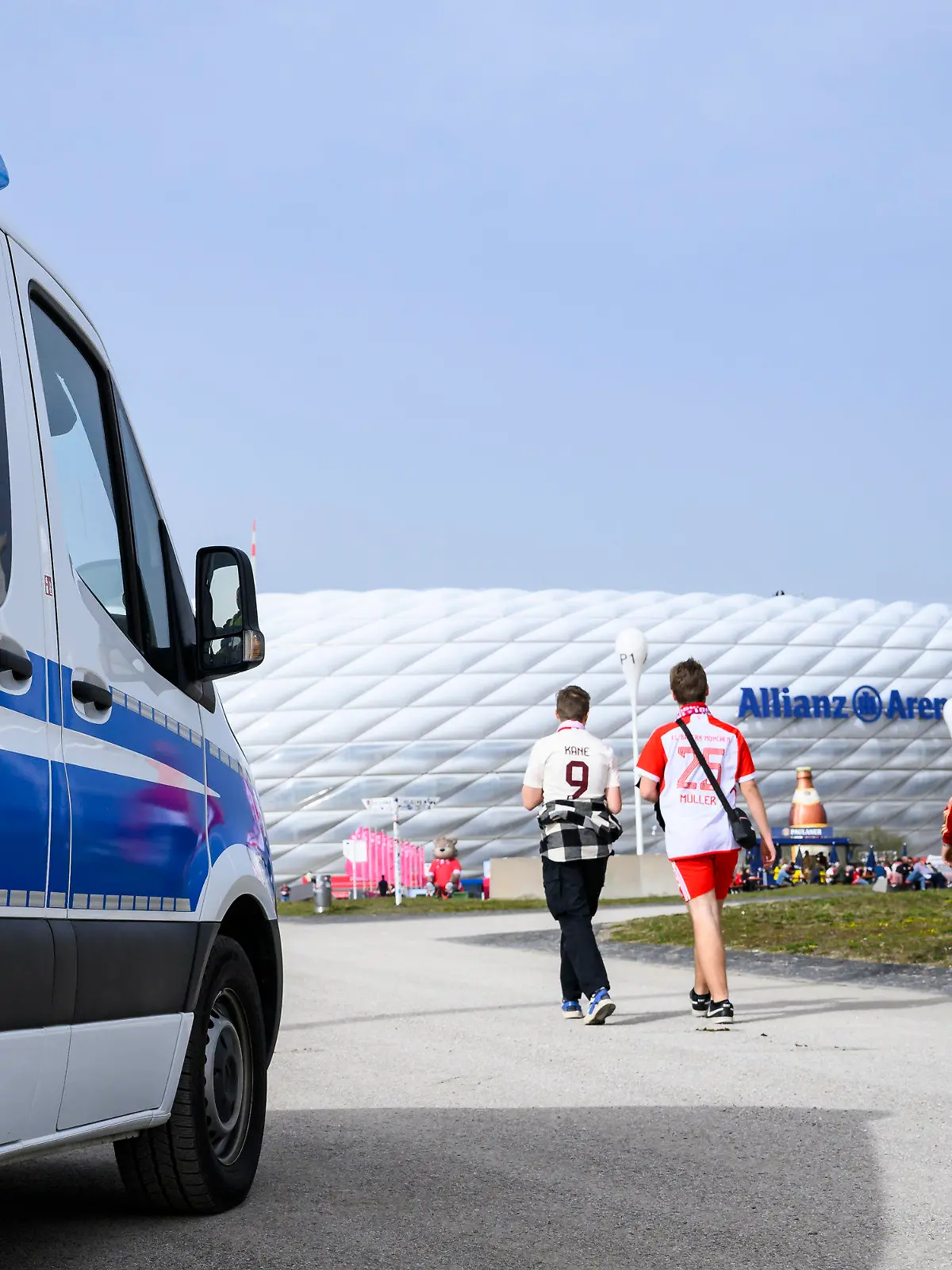 dpatopbilder - 30.03.2024, Bayern, München: Fußball: Bundesliga, Bayern München - Borussia Dortmund, 27. Spieltag, Allianz Arena. Fans gehen neben einem Auto der Polizei vor dem Spiel in die Allianz Arena. Foto: Tom Weller/dpa - WICHTIGER HINWEIS: Gemäß den Vorgaben der DFL Deutsche Fußball Liga bzw. des DFB Deutscher Fußball-Bund ist es untersagt, in dem Stadion und/oder vom Spiel angefertigte Fotoaufnahmen in Form von Sequenzbildern und/oder videoähnlichen Fotostrecken zu verwerten bzw. verwerten zu lassen. +++ dpa-Bildfunk +++