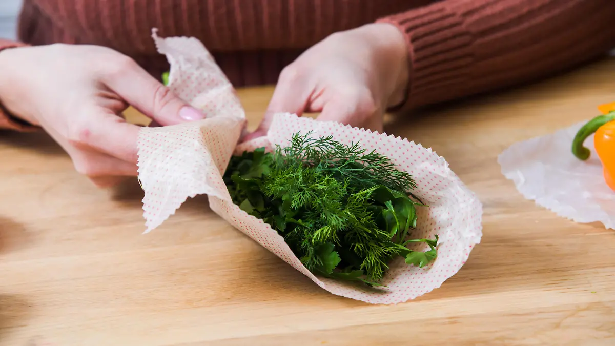Female wrapping green dill and parsley into beeswax wraps. Zero waste kitchen with reused packaging materials. Scandinavian style kitchen || Modellfreigabe vorhanden