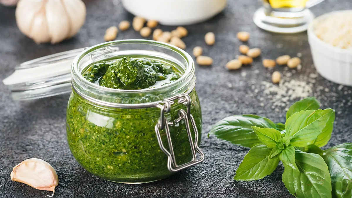 Homemade pesto sauce and ingredients on dark cement background. Close up wiev of basil pesto in glass jar with ingredients.