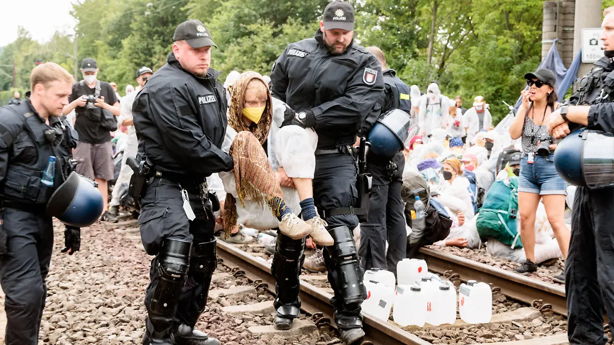 13.08.2022, Hamburg: Klima-Aktivisten die aus Protest Gleise im Hamburger Hafen besetzt haben, werden einzeln von Polizeibeamten von den Gleisen getragen. Klimaaktivisten haben in Hamburg an verschiedenen Stellen Blockaden initiiert, um für mehr Klimagerechtigkeit zu protestieren. Etwa 400 Klima-Aktivisten haben am Samstag den Hamburger Hafen lahmgelegt. Sie besetzten seit dem Mittag die einzige Bahnstrecke zum Containerterminal, wie das Aktionsbündnis «Ende Gelände» mitteilte. Foto: Markus Scholz/dpa +++ dpa-Bildfunk +++