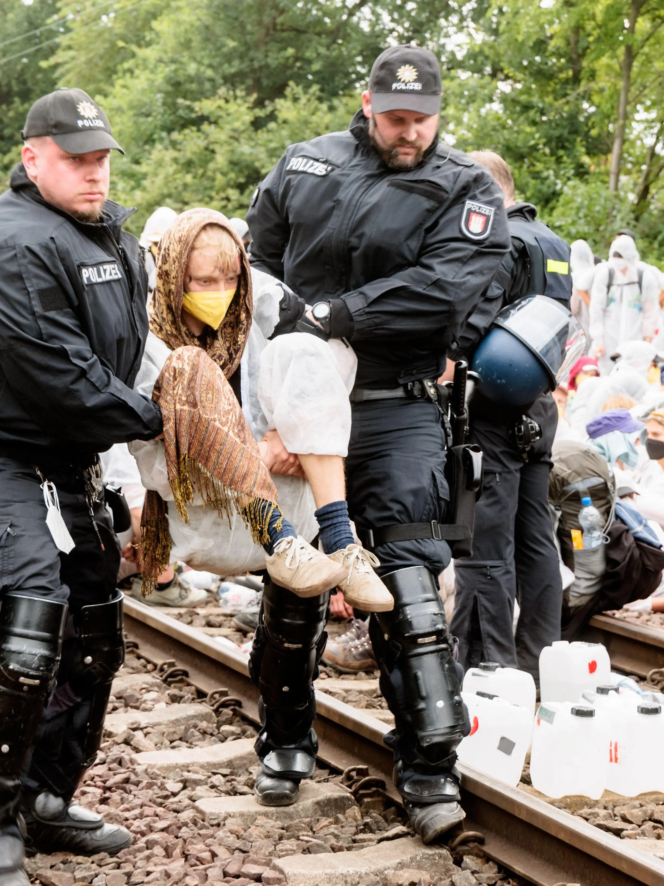 13.08.2022, Hamburg: Klima-Aktivisten die aus Protest Gleise im Hamburger Hafen besetzt haben, werden einzeln von Polizeibeamten von den Gleisen getragen. Klimaaktivisten haben in Hamburg an verschiedenen Stellen Blockaden initiiert, um für mehr Klimagerechtigkeit zu protestieren. Etwa 400 Klima-Aktivisten haben am Samstag den Hamburger Hafen lahmgelegt. Sie besetzten seit dem Mittag die einzige Bahnstrecke zum Containerterminal, wie das Aktionsbündnis «Ende Gelände» mitteilte. Foto: Markus Scholz/dpa +++ dpa-Bildfunk +++