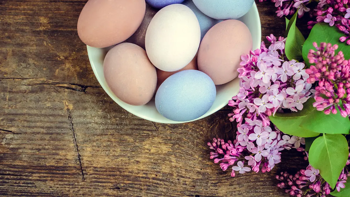 Easter background with handmade painted purple eggs and lilac on a wooden vintage board with place for text. Top view. Copy space.