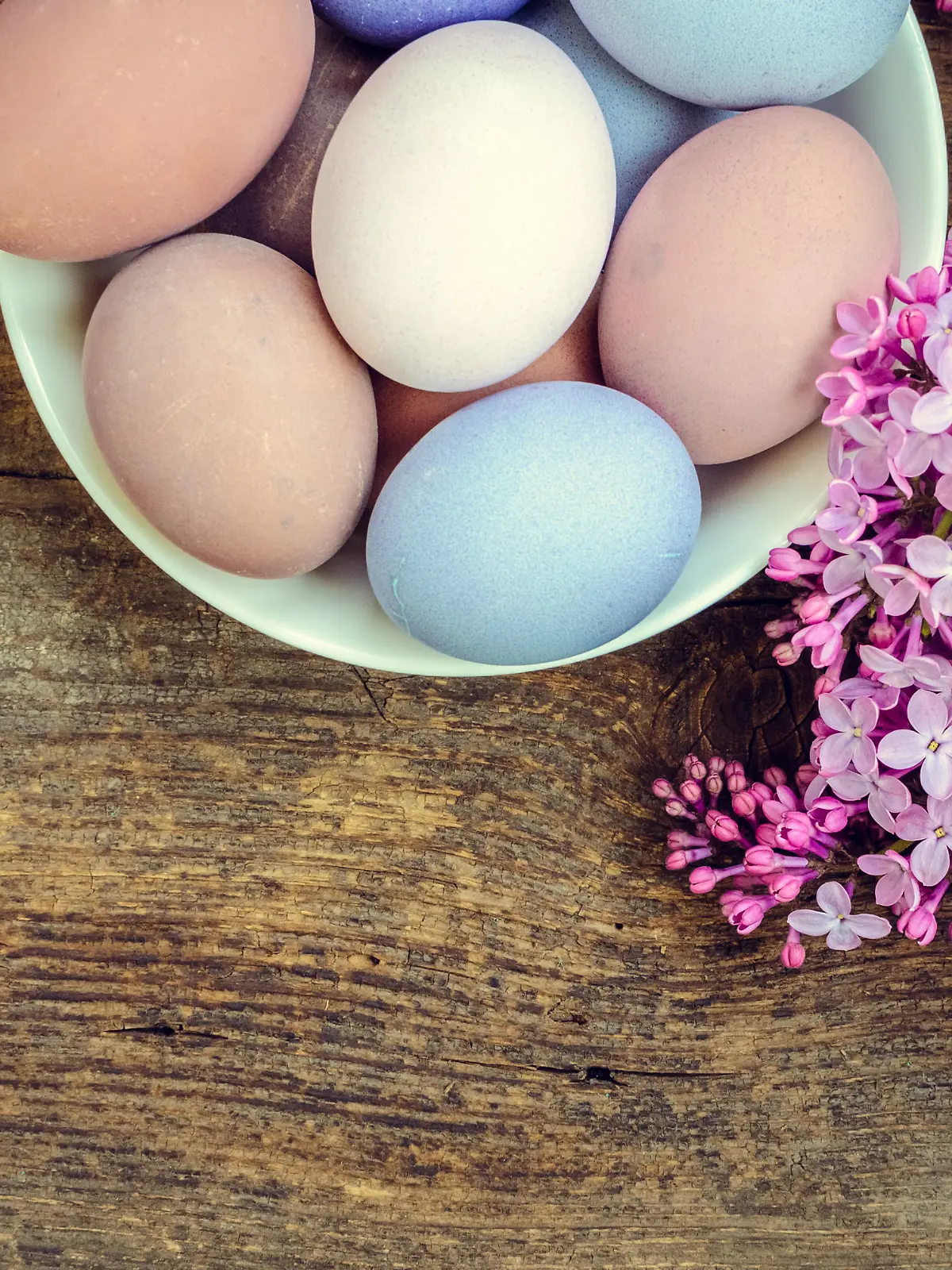 Easter background with handmade painted purple eggs and lilac on a wooden vintage board with place for text. Top view. Copy space.