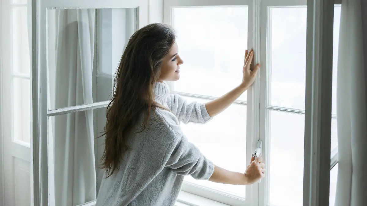 Woman is opening window to look at beautiful snowy landscape outside