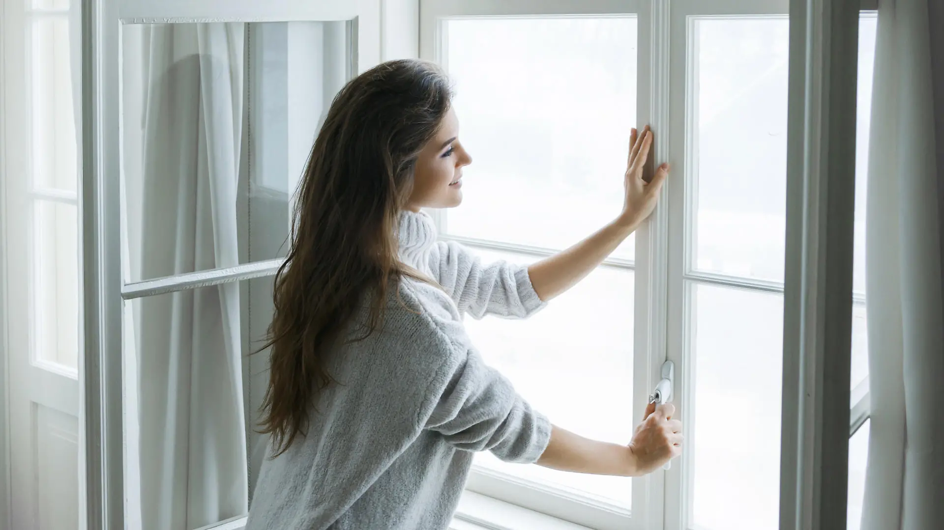 Woman is opening window to look at beautiful snowy landscape outside