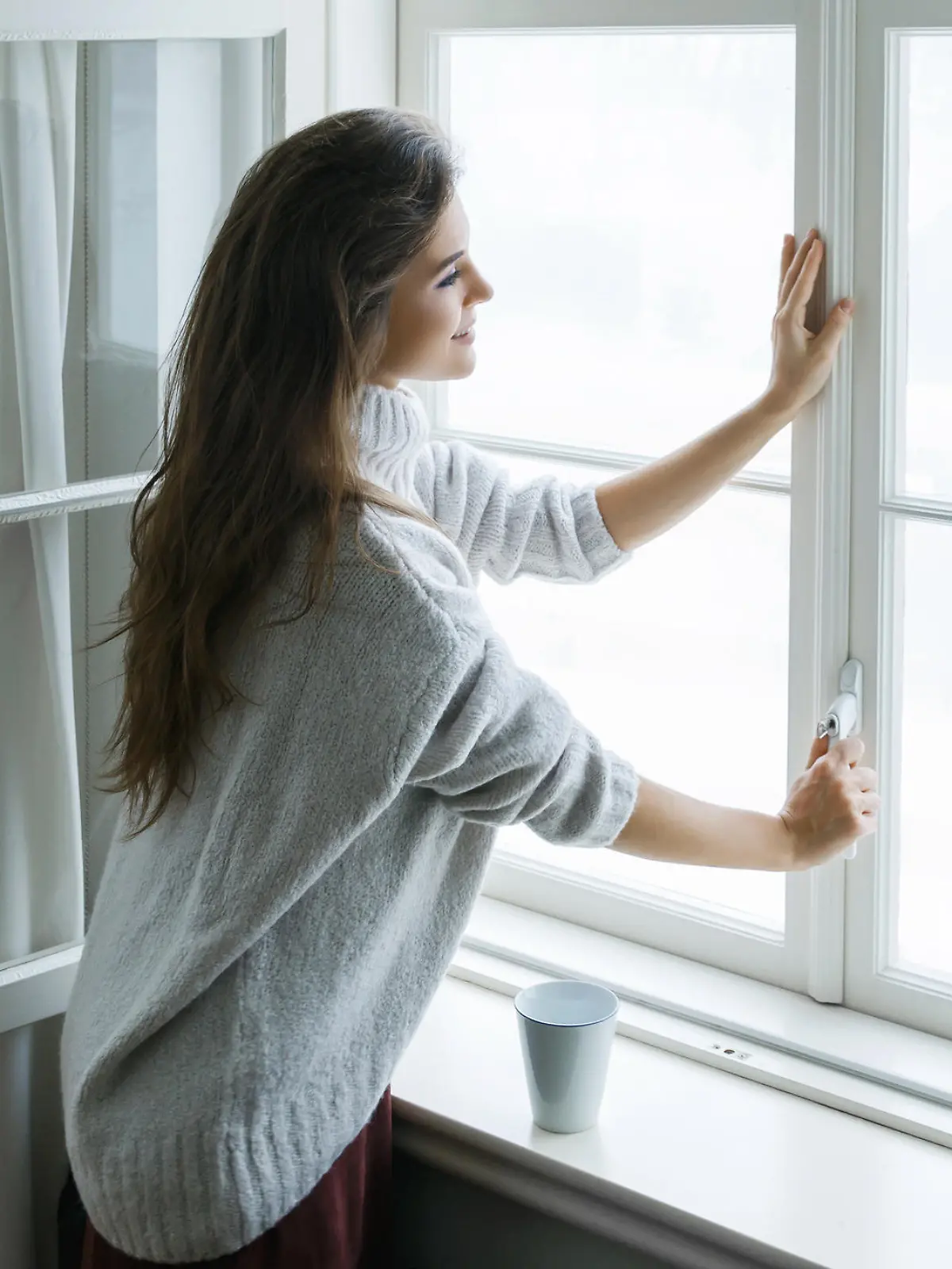 Woman is opening window to look at beautiful snowy landscape outside