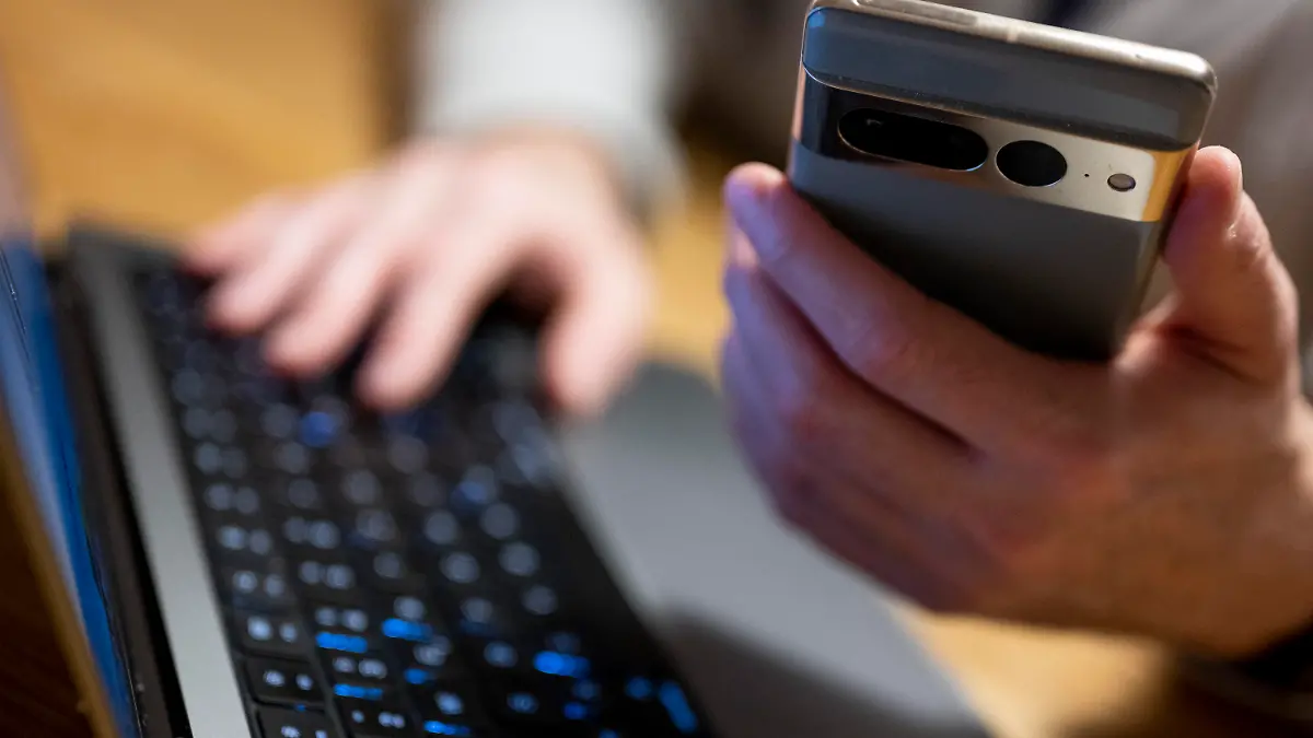 ILLUSTRATION - 27.02.2023, Berlin: Ein Mann sitzt am Laptop und hält ein Smartphone mit in der Hand. (zu dpa: «Mann will Geld investieren und wird um 75 000 Euro betrogen») Foto: Monika Skolimowska/dpa +++ dpa-Bildfunk +++