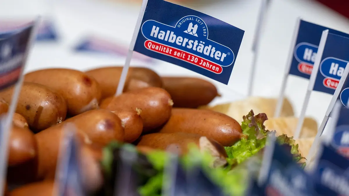 Ein Papierfähnchen mit dem Logo der Marke Halberstädter steckt in einem Würstchen am Stand des Herstellers auf der Grünen Woche.