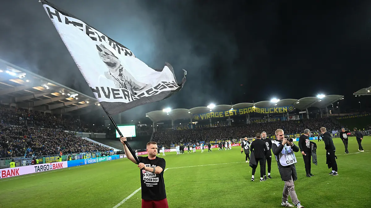 SAARBRUECKEN, GERMANY - APRIL 02: Jean Zimmer of 1. FC Kaiserslautern celebrates after the team's victory with a flag during the DFB Cup semifinal match between 1. FC Saarbrücken and 1. FC Kaiserslautern at the Ludwigsparkstadion on April 02, 2024 in Saarbruecken, Germany. (Photo by Christian Kaspar-Bartke/Getty Images)