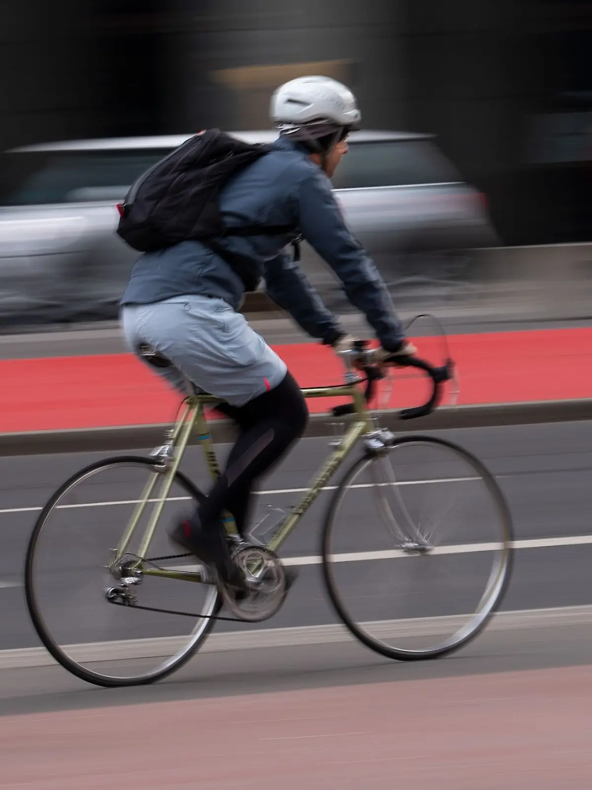 Ein Fahrradfahrer mit Helm fährt über einen Radweg an der Straße.