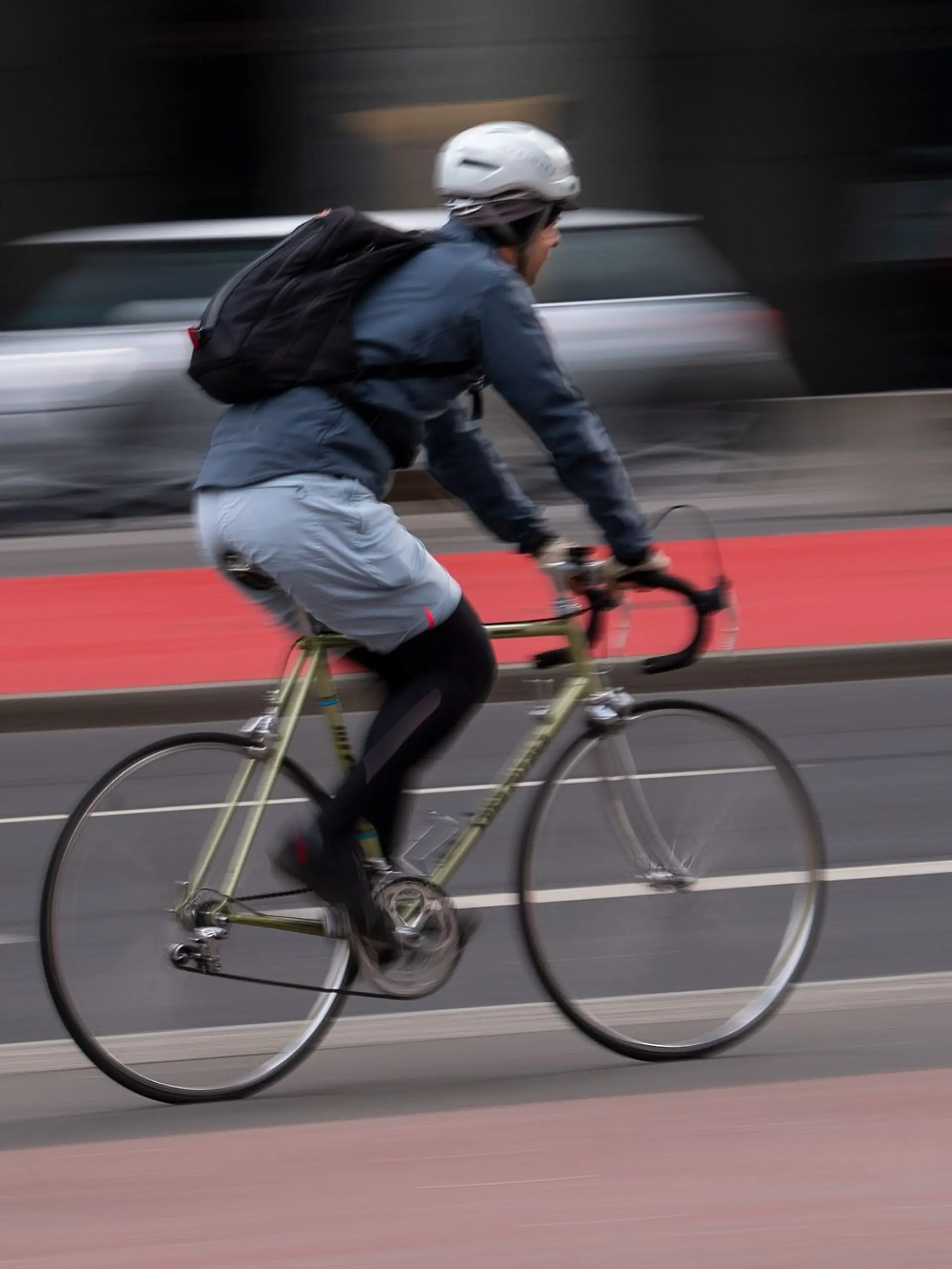 Ein Fahrradfahrer mit Helm fährt über einen Radweg an der Straße.
