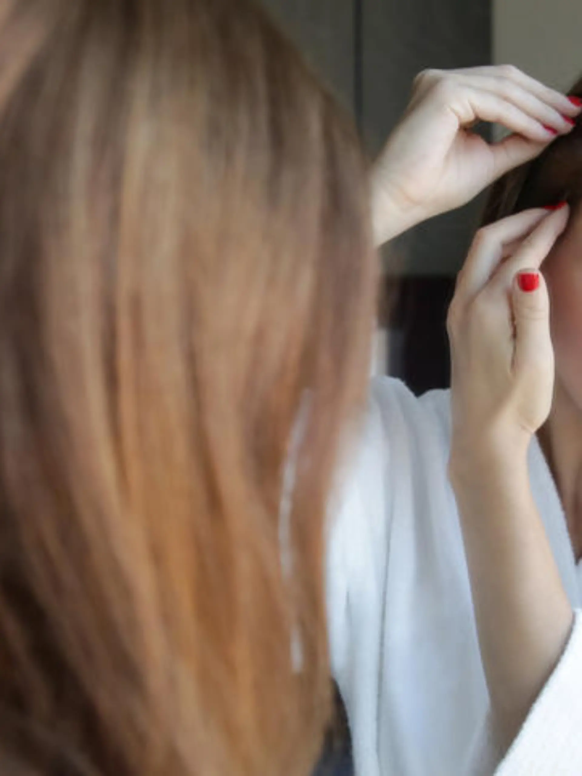 Portrait of a beautiful young woman examining her scalp and hair in front of the mirror, hair roots, color, grey hair, hair loss or dry scalp problem