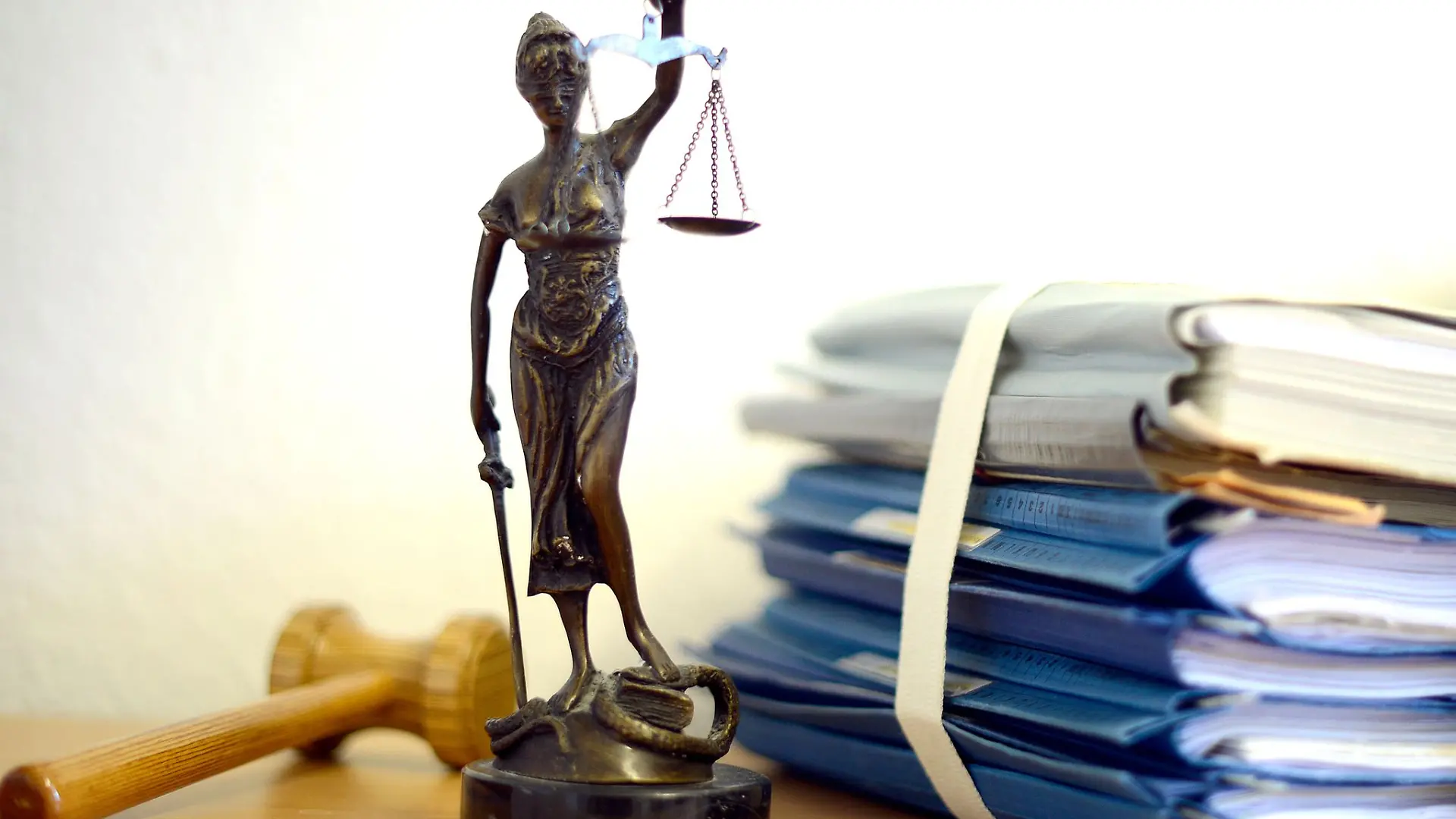 Die modellhafte Nachbildung der Justitia steht in einem Raum eines Richters neben einem Holzhammer und einem Aktenstapel.