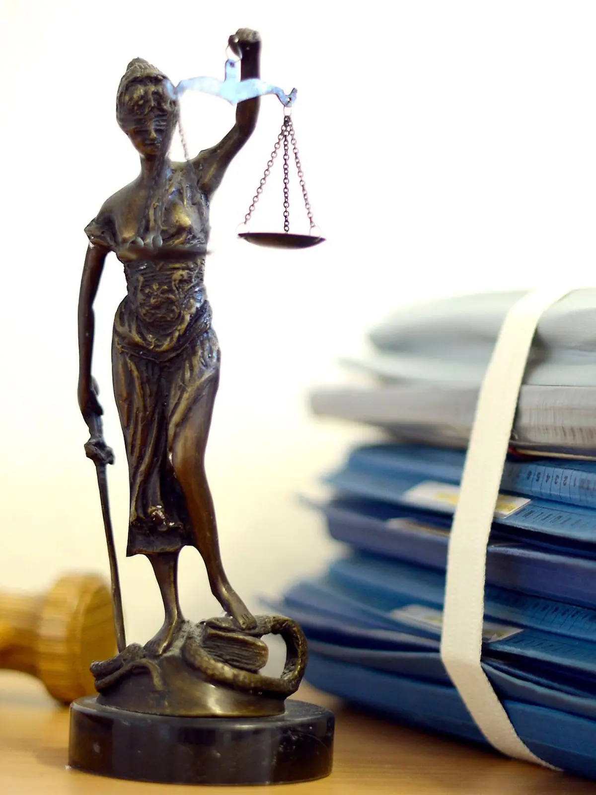 Die modellhafte Nachbildung der Justitia steht in einem Raum eines Richters neben einem Holzhammer und einem Aktenstapel.