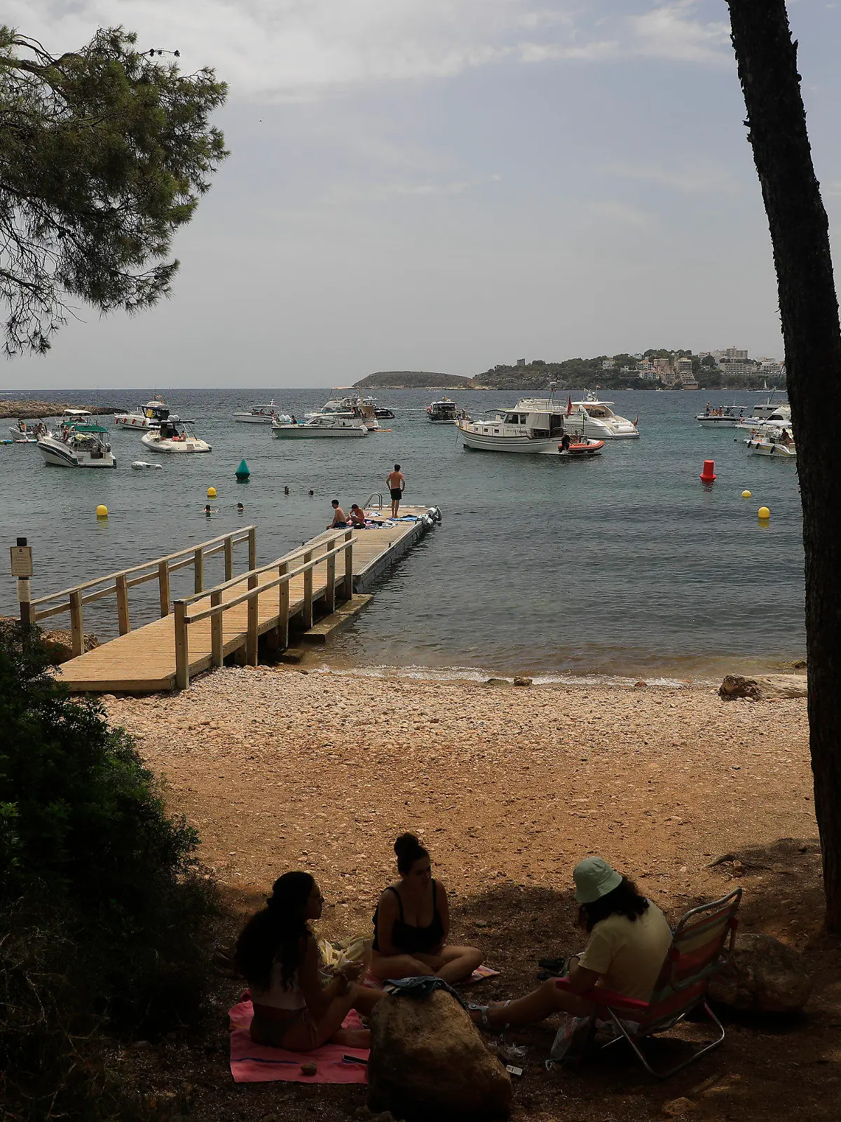22.07.2023, Spanien, Calvia: Menschen entspannen sich am Strand von Punta Negra auf Mallorca, wo mehrere Schiffe ankern. Das Mittelmeer erwärmt sich einer Studie zufolge immer schneller und wird dabei auch immer salziger. Das Wasser erwärme sich infolge des Klimawandels mit einer Geschwindigkeit von etwa zwei Grad je 100 Jahre im westlichen Mittelmeer und an einigen Stellen sogar um drei Grad pro Jahrhundert, schrieben Wissenschaftler des spanischen Meeresforschungsinstituts ICM-CSIC in der Zeitschrift «Journal of Marine Science and Engineering». Foto: Clara Margais/dpa +++ dpa-Bildfunk +++