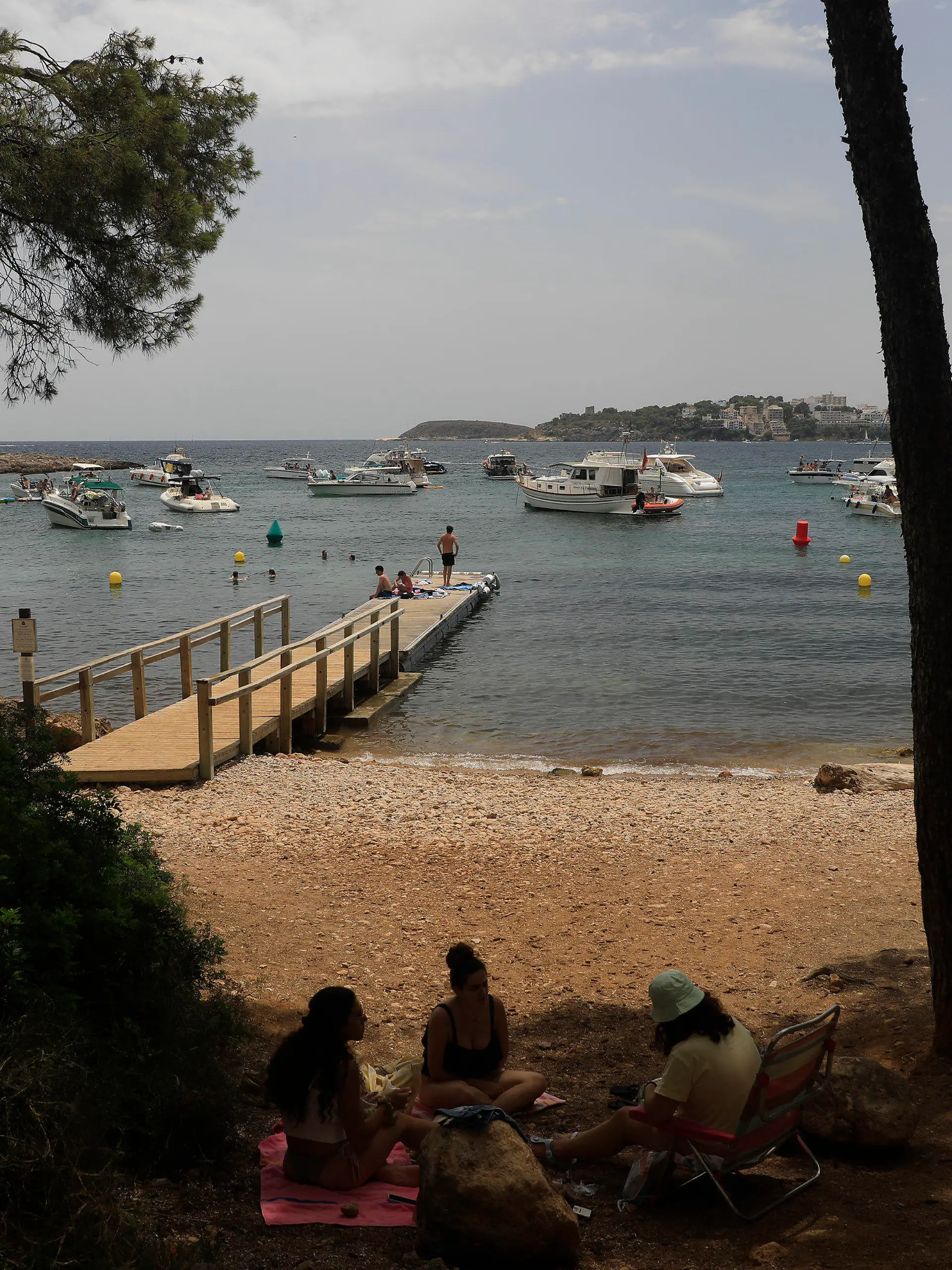 22.07.2023, Spanien, Calvia: Menschen entspannen sich am Strand von Punta Negra auf Mallorca, wo mehrere Schiffe ankern. Das Mittelmeer erwärmt sich einer Studie zufolge immer schneller und wird dabei auch immer salziger. Das Wasser erwärme sich infolge des Klimawandels mit einer Geschwindigkeit von etwa zwei Grad je 100 Jahre im westlichen Mittelmeer und an einigen Stellen sogar um drei Grad pro Jahrhundert, schrieben Wissenschaftler des spanischen Meeresforschungsinstituts ICM-CSIC in der Zeitschrift «Journal of Marine Science and Engineering». Foto: Clara Margais/dpa +++ dpa-Bildfunk +++
