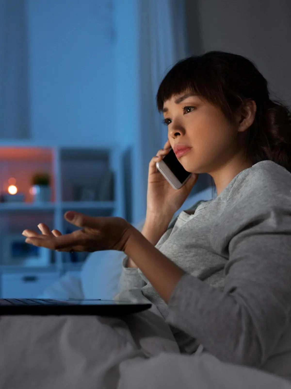 technology, internet, communication and people concept - stressed young asian woman with laptop computer calling on smartphone in bed at home at night || Modellfreigabe vorhanden