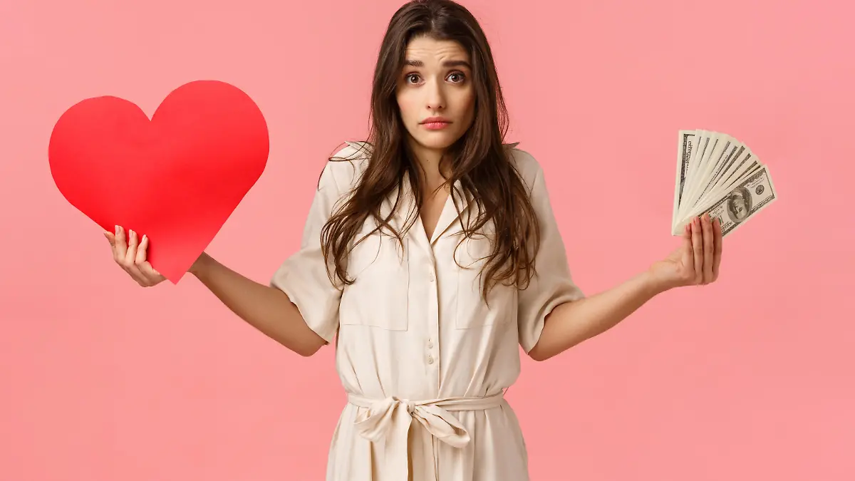 Indecisive and unsure, cute lovely modern woman cant decide what important, shrugging looking confused camera, holding heart card and money, dont know whats right, questioned over pink background.
