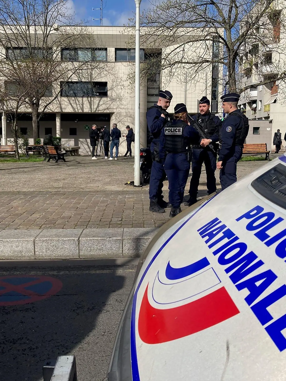 18.03.2024, Frankreich, La Courneuve: Polizisten und Journalisten stehen vor einem Polizeirevier in einem nördlichen Vorort von Paris. Einen Tag zuvor war die Wache Ziel eines Brandanschlags. Nach dem Tod eines 18-Jährigen bei einem Polizeieinsatz bei Paris hatten Dutzende junge Leute am späten Sonntagabend die Wache mit Feuerwerkskörpern und Molotowcocktails attackiert. Foto: Clotilde Gourlet/AFP/dpa +++ dpa-Bildfunk +++