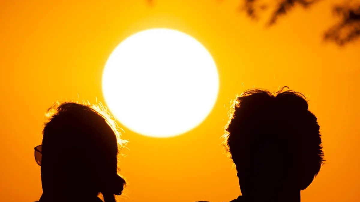 Zwei Personen beobachten vom Gipfelplateau des Großen Feldberg im Taunus aus, wie die Sonne am Horizont untergeht.