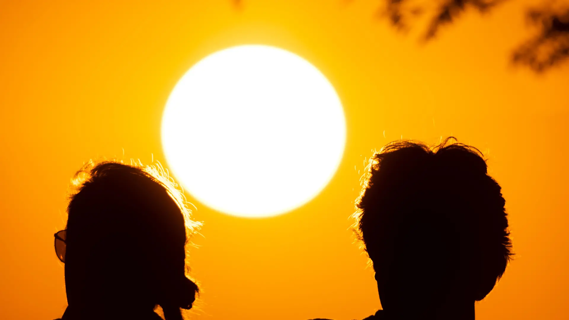 Zwei Personen beobachten vom Gipfelplateau des Großen Feldberg im Taunus aus, wie die Sonne am Horizont untergeht.