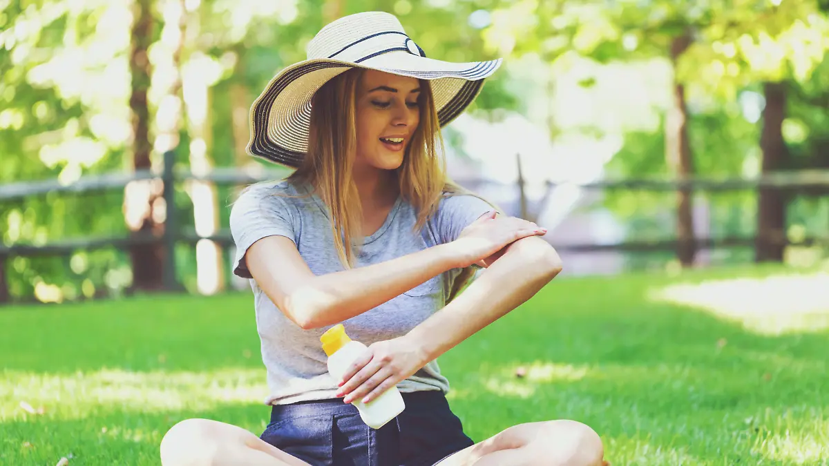 Young woman a bottle of sunblock outside on a summer day