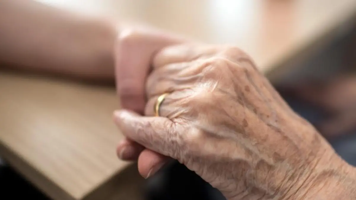Eine Pflegerin hält die Hand einer alten Frau in einem Altenheim
